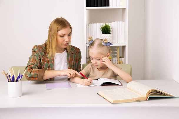 Мати робить домашнє завдання з дочкою в приміщенні, сидячи на столі
. - Фото, зображення