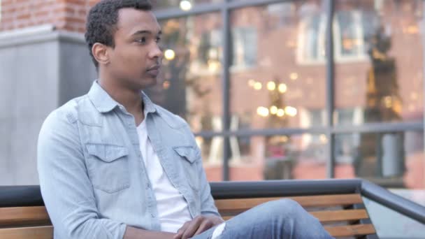 Νέος Αφρικανός άνθρωπος χαμογελά ενώ κάθεται στο παγκάκι - Πλάνα, βίντεο