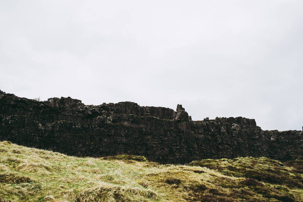 春のアイスランドのシングヴェリル国立公園の冷たい荒涼とした風景。暗い霧の山々と灰色の空に対する古代の岩. - 写真・画像