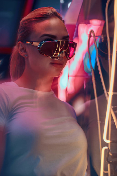 Atraktivní styltivá žena se pózuje pro fotografa v neonové světelné světlici. Na pozadí je tma. - Fotografie, Obrázek