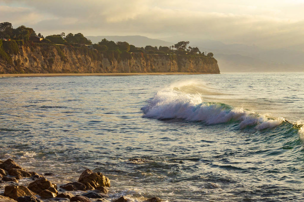 onda di rottura con schiuma e backwash curva attraverso baia a penensulla e spiaggia lontana con litorale roccioso, all'alba
  - Foto, immagini