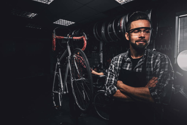 Przystojny Brodaty mężczyzna w okularach stoi w pobliżu stałego roweru w swoim warsztacie - Zdjęcie, obraz