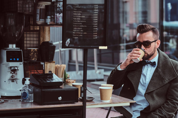 Atrakcyjny elegancki mężczyzna w okulary pije kawę siedząc na zewnątrz w Coffeeshop - Zdjęcie, obraz