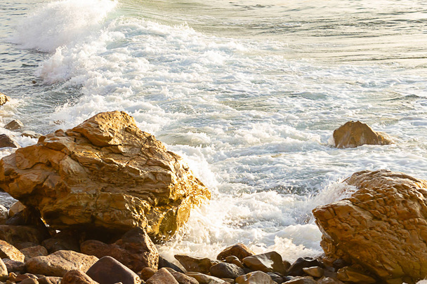 foaming wave breaking at sunrise with rocky shoreline - Photo, Image