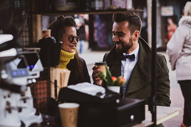 Atractiva pareja inteligente está disfrutando del café mientras se sienta afuera en el pequeño coffeesho
 - Foto, imagen