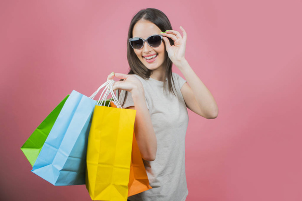 Portrait of an excited beautiful girl wearing  sunglasses holding shopping bags  - Foto, afbeelding