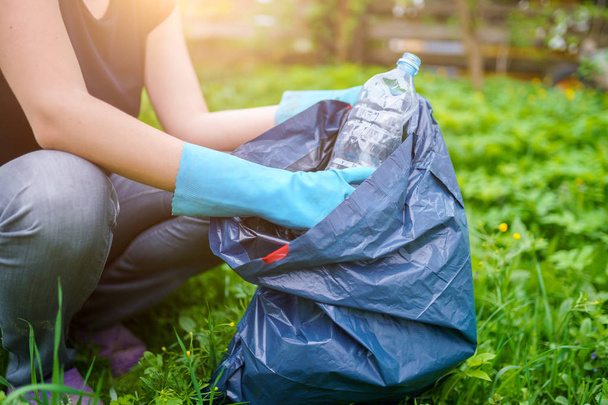 Image of woman in rubber gloves picking up dirty plastic bottle on lawn - Фото, зображення