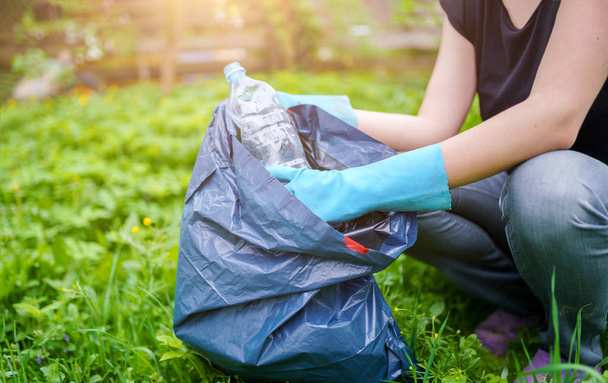 Picture of woman in rubber gloves picking up dirty plastic bottle on lawn - Photo, image