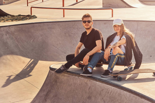 Cool trendy students are sitting at sunny skatepark with their longboards - Photo, Image