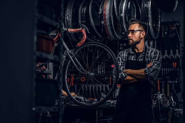 Przystojny mężczyzna w okularach stoi w pobliżu stałego roweru w swoim warsztacie. - Zdjęcie, obraz