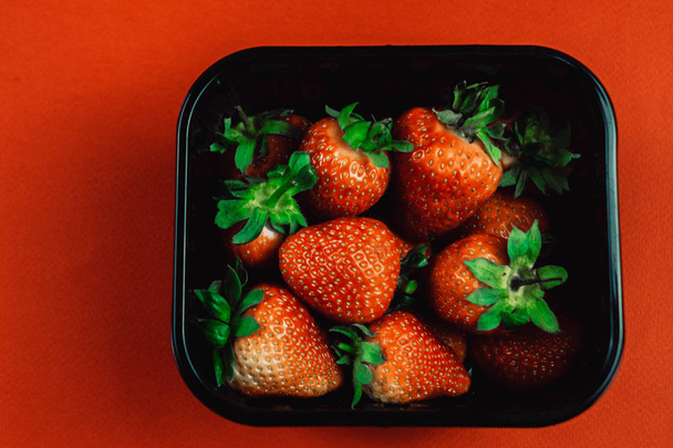 Fresh juicy strawberries with leaves in a black basket. Strawberry on a red background - Fotoğraf, Görsel
