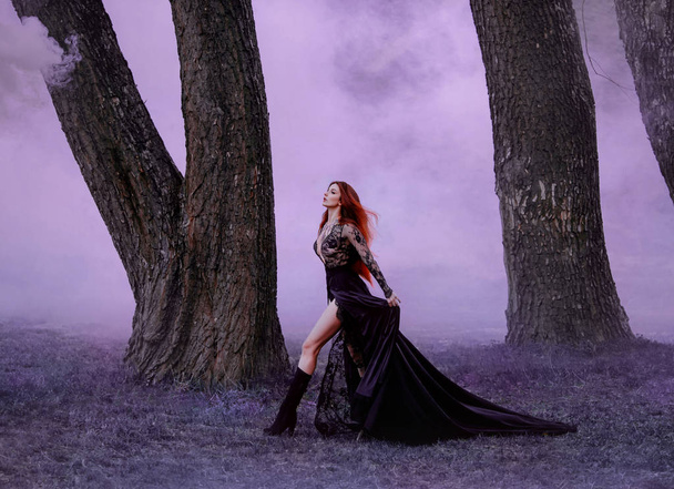 Seductive vampire defiantly goes baring beautiful long legs. Ginger witch in a black silk dress with a long train, runs in the purple fog, hair fluttering in the wind. Countess Dracula. Art processing - Fotografie, Obrázek
