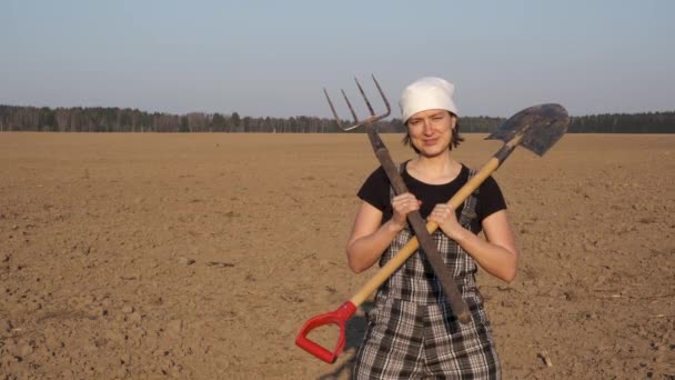 Portrait of female farmer with shovel and pitchfork on freshly plowed field on sunset. - Video, Çekim