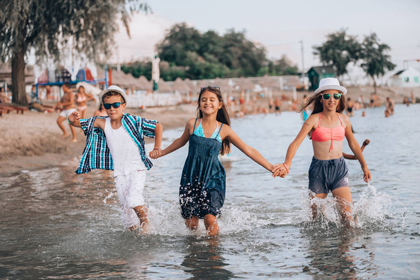 Onnelliset lapset juoksevat yhdessä veden halki ja pitävät toisiaan kädestä
  - Valokuva, kuva