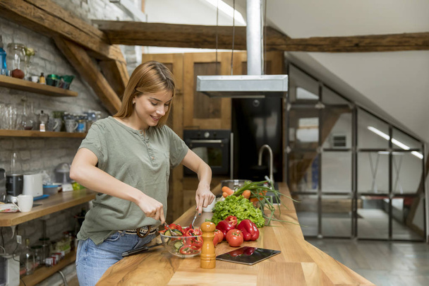 Szczęśliwa młoda kobieta gotowanie pyszne i zdrowe jedzenie w kuchni na poddaszu w rustykalny Apartament - Zdjęcie, obraz