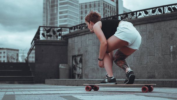 Beautiful young girl with tattoos sits on longboard - Fotó, kép