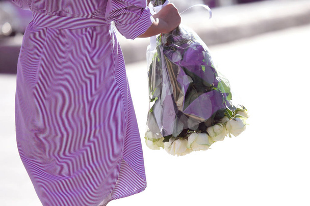 meisje in een blauw gestreepte jurk wordt geleverd met een boeket van witte rozen - Foto, afbeelding