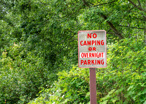 Brak kempingu lub nocny znak parkowania z czerwonym napisem na wiejskiej drodze obok zielonych drzew. - Zdjęcie, obraz
