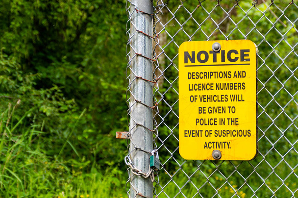 Segnale di allarme giallo e nero quartiere crimine pubblicato sulla recinzione di collegamento a catena con sfondo boscoso
. - Foto, immagini