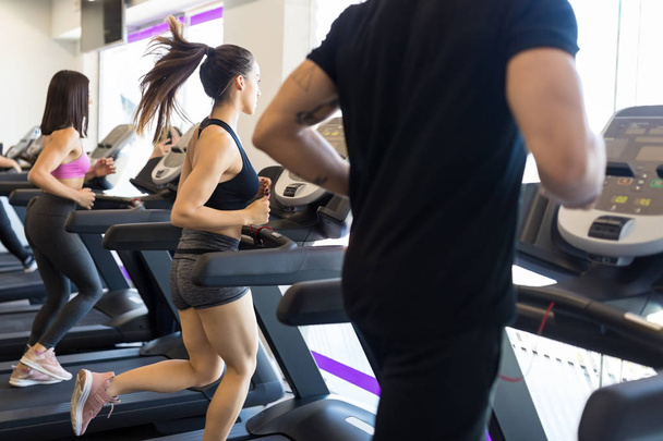 Amis masculins et féminins faisant de l'exercice sur tapis roulant dans la salle de gym moderne
 - Photo, image