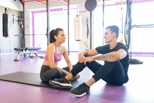 Sportieve vrouw praat met instructeur tijdens pauze in het fitnesscentrum - Foto, afbeelding