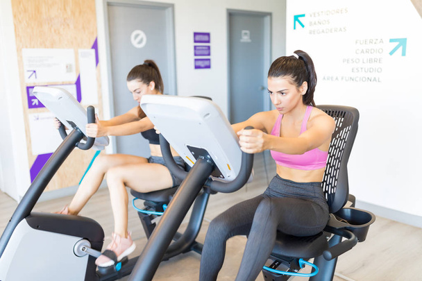 Young and beautiful women using spin machines in gym - Photo, Image
