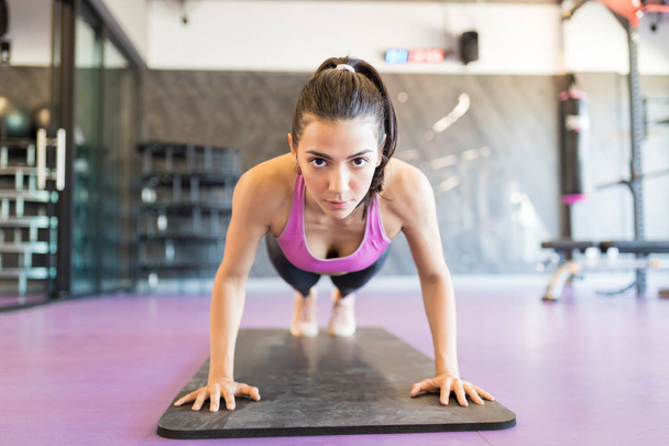 Hispanic woman exercising push ups and making eye contact at fitness club - Фото, изображение