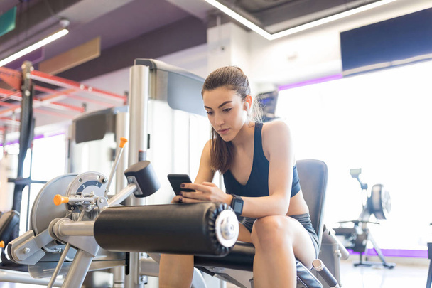 Good looking woman texting on smartphone after workout in fitness gym - Fotó, kép