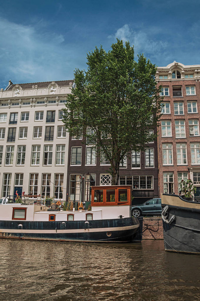 Старые кирпичные здания возле канала с пришвартованными лодками в Амстердаме
 - Фото, изображение