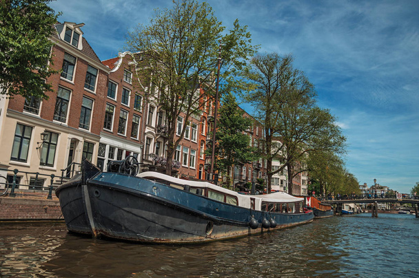 Старые кирпичные здания возле канала с пришвартованными лодками в Амстердаме
 - Фото, изображение