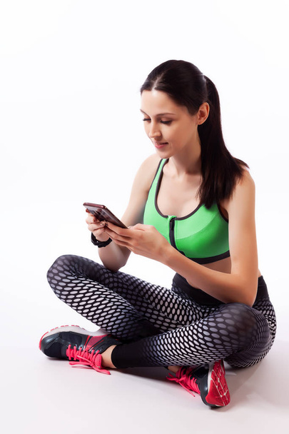 A sport woman  having break during jogging exercise, monitoring her route on mobile phone   on a  white isolated background in studio. Woman runner using running app on gadget to track her progress  - 写真・画像