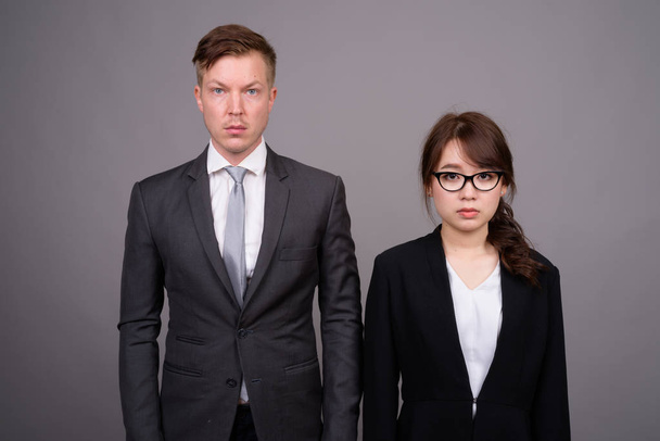 Joven hombre de negocios y joven mujer de negocios asiática contra bac gris
 - Foto, Imagen
