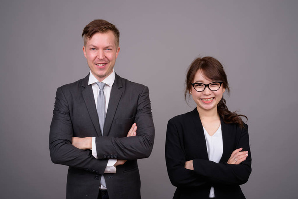 Young businessman and young Asian businesswoman against gray bac - Foto, immagini