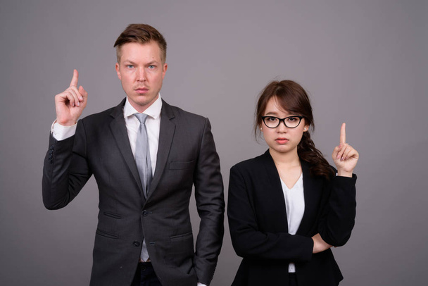 Young businessman and young Asian businesswoman against gray bac - Foto, Imagem