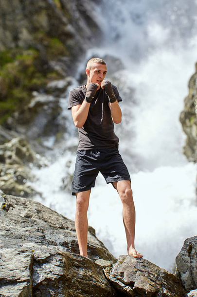 Muay Thai fighter training with shadow boxing by strong waterfall - Fotoğraf, Görsel
