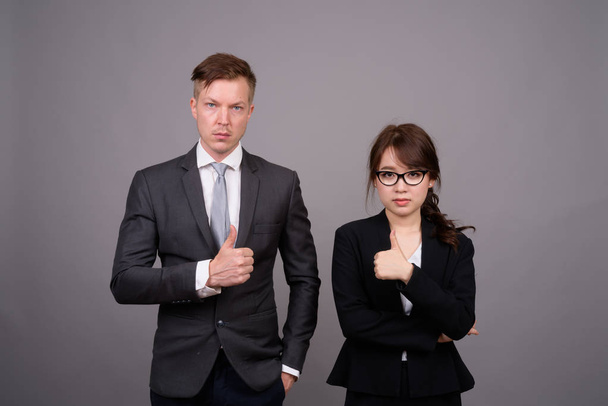 junge Geschäftsfrau und junge asiatische Geschäftsfrau gegen grauen Bac - Foto, Bild