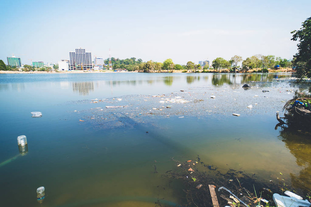 Ρύπανση του περιβάλλοντος στην πόλη, ανθρώπινα απόβλητα. Σκουπίδια στη λιμνούλα στο φόντο των σπιτιών της πόλης. - Φωτογραφία, εικόνα