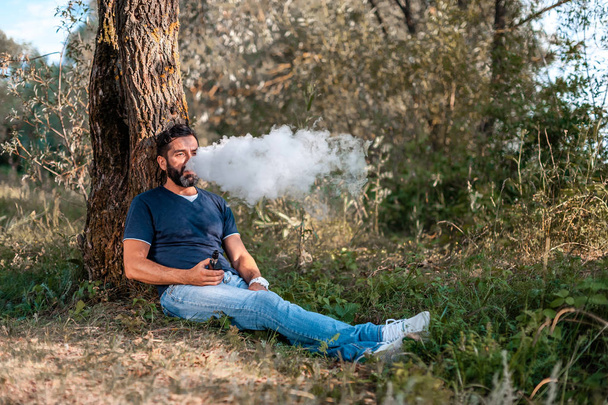 Szakállas férfi felrobban egy pár elektronikus cigaretta az erdei földön. Megszabadulni a nikotin-függőség. - Fotó, kép