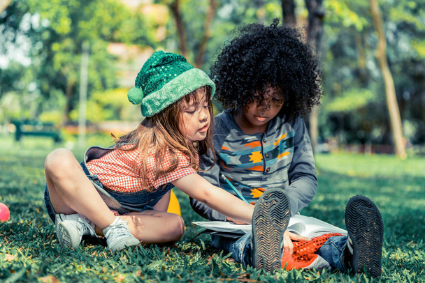 Школьный мальчик и девочка вместе читают книгу в парке
. - Фото, изображение