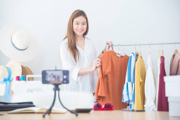 Красивая женщина-блоггер показывает одежду перед камерой для записи видео видеоблога в прямом эфире в своем магазине
 - Фото, изображение