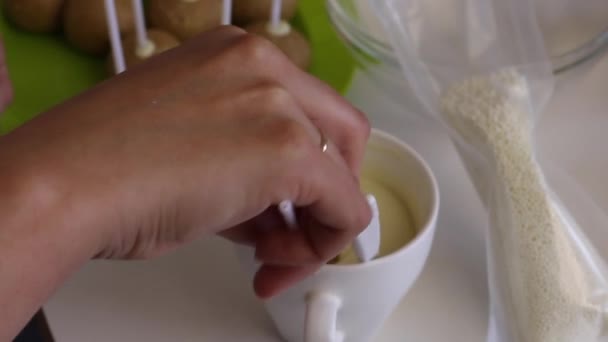 A woman dips a popcake billet into melted white chocolate. Spreads the glaze evenly. - Video