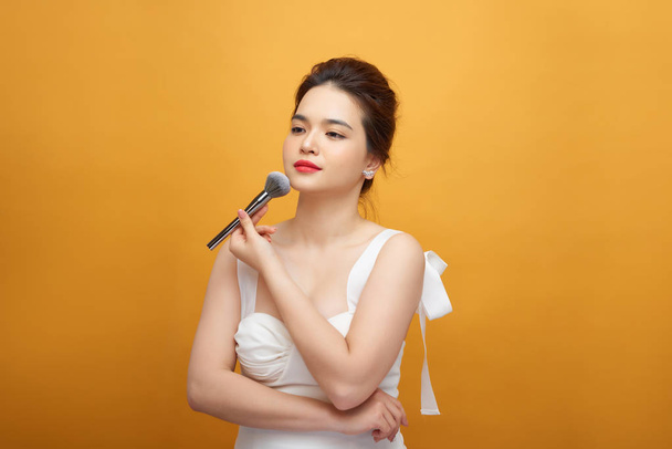 hermosa mujer sosteniendo maquillaje cepillo sobre amarillo - Foto, Imagen