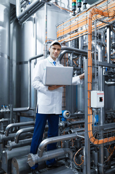 Portrait d'homme en robe blanche et un chapeau debout dans le département de production de l'usine laitière avec ordinateur portable
 - Photo, image