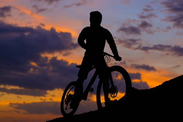 Radler in kurzen Hosen und Trikot auf einem modernen Carbon-Hardtail-Bike mit Luftfederung fährt im Sommer bei Sonnenuntergang auf den orangeroten Hügeln im Gelände - Foto, Bild