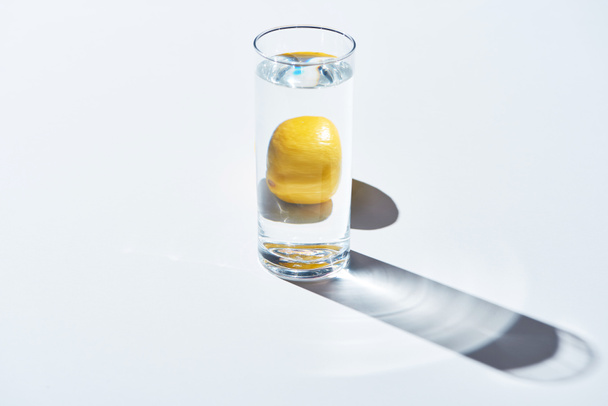 transparent glass with water and whole lemon on white background  - Valokuva, kuva