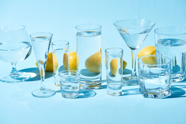 transparent glasses with water and whole lemons on blue background  - Photo, Image