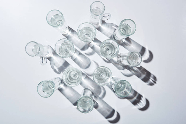 top view of glasses with clear water and shadows on white surface - 写真・画像
