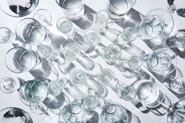 top view of glasses with pure water and shadows on white surface - Fotoğraf, Görsel