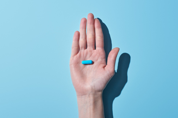 cropped view of woman holding blue pill on palm on blue background - Foto, imagen