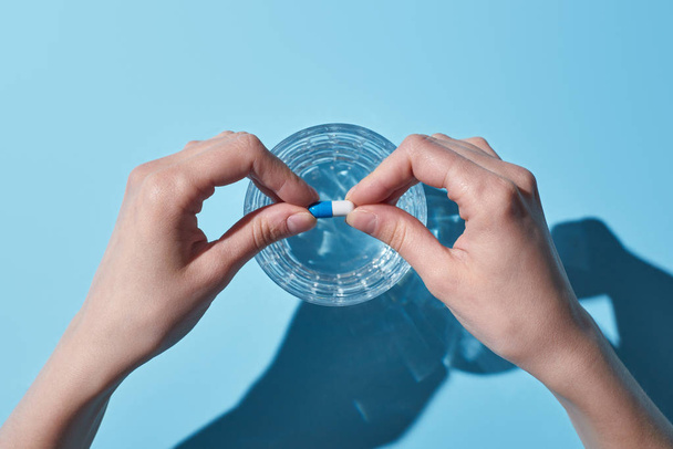 visão parcial da mulher colocando pílula em vidro com água no fundo azul
 - Foto, Imagem